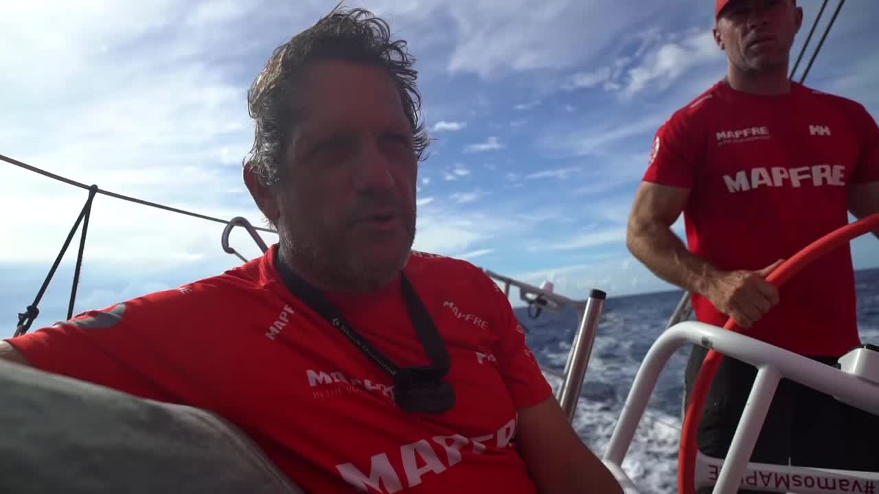 Joan talks in Spanish about the Solomons, wind, squalls, complicated strategy, Dongfeng ahead, and the other boats behind them. Xabi talks about how they've been in this situation before, lead by Dongfeng through much of the leg. "Now we've gained as much as possible, and wait for our opportunity." Talks about the doldrums coming up. Night shot of distant lightning silhouetting the helmsman. In the day, Xabi in the pit. Shot of Dongfeng ahead of them and to port with an island below them. Stacking. Green island to leeward. Pablo grinds with an island below them. Stacking forward. Shot astern with a whale surfacing; then slomo of the whale surfacing. AkzoNobel behind them. Dongfeng ahead and to weather. Light winds. AkzoNobel close behind them. Willy looking through binoculars. Drone shot of a fishing boat with a purse seine and MAPFRE in the background. Circling drone shot of MAPFRE with Dongfeng visible in 3 miles away, ahead and to weather.
