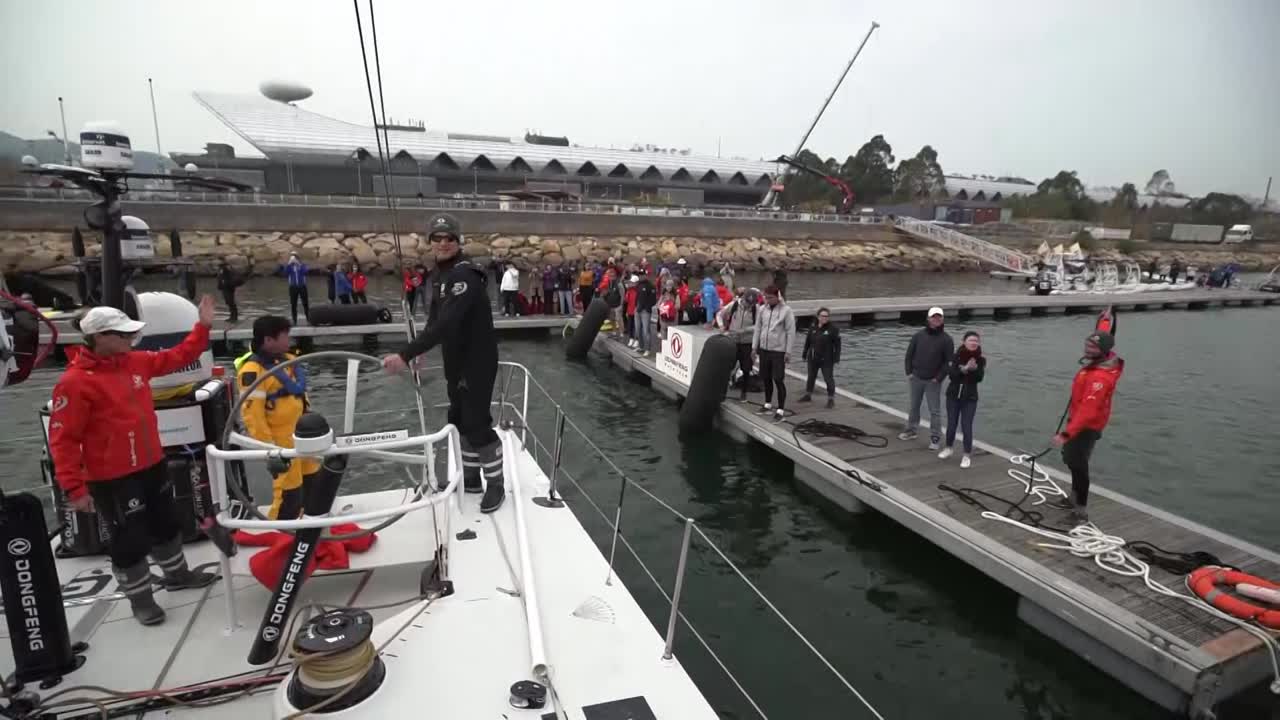Dongfeng docking out at the start of Leg 6. Black waves goodbye to the people on the dock. We see the MH0 being unfurled as Charles steers on the approach to the starting line. AkzoNobel is visible ahead of them and to leeward, the rest of the fleet to weather. Pascal with a tablet in his hand. Jérémie, after the start, looking forward at AkzoNobel and Brunel ahead of them. We see them furling the MH0 for a tack from port to starboard, then unfurling during a tack back to port. Charles: "Nice one." Pascal navigating. Their jumper going over. Kevin standing on the lifelines to do something to the clew of the MH0. Passing the leaving buoy. Later, they prepare to peel to the J1. Daryl: "Put the sheet around the winch." Bagging the lowered MH0 on the foredeck. Charles on the helm, talks about the start. Not so great in terms of their start, but good to have wind in exiting Hong Hong. Now at the back of the fleet. Daryl: "Looking forward to sailing into Auckland. Probably 20 days away. Don't want to get too excited yet." Jack, stacking on the foredeck, says pretty much the same thing. "Long way to go though."